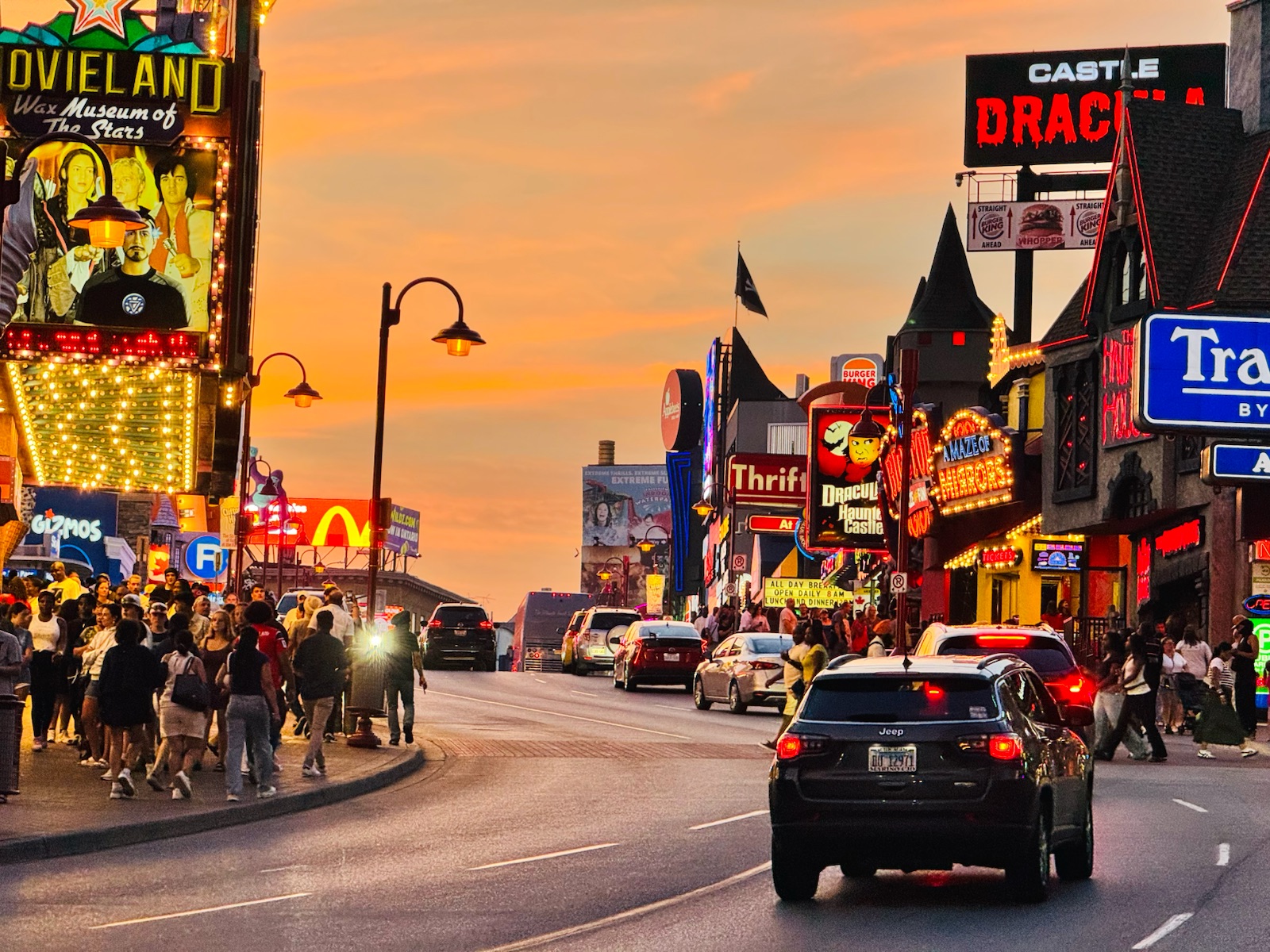 A busy street of neon signs and crowds at sunset