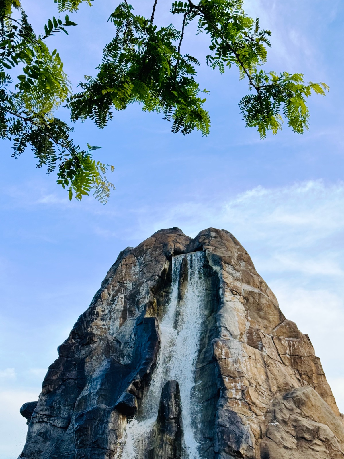 A rock peak with a waterfall, framed by leaves